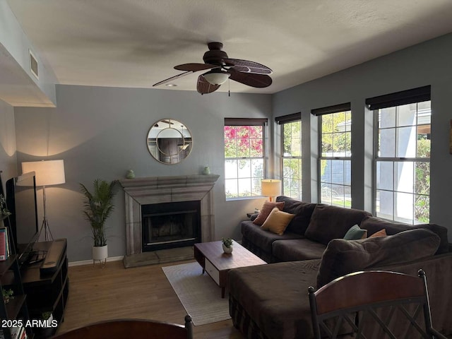 living area with ceiling fan, visible vents, a fireplace with raised hearth, wood finished floors, and baseboards
