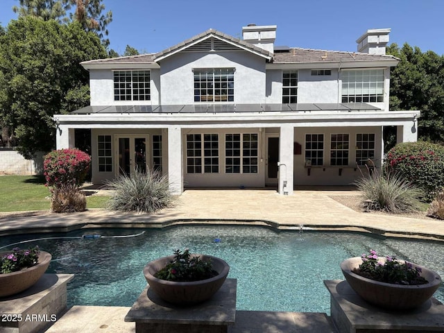 rear view of property featuring a patio, stucco siding, a chimney, an outdoor pool, and french doors