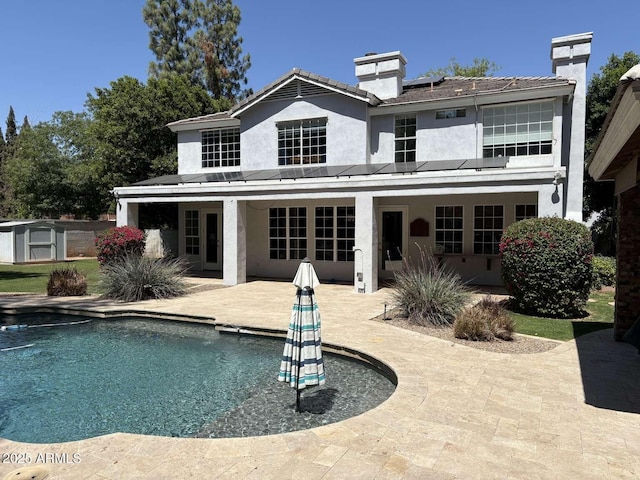 rear view of property featuring a patio area, an outdoor pool, stucco siding, and a chimney