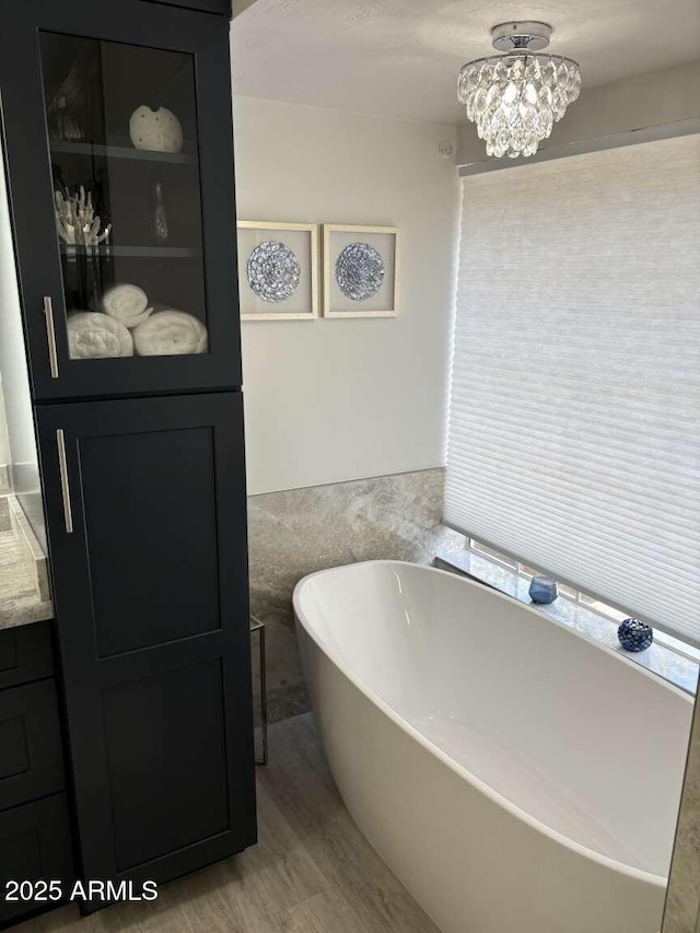 bathroom featuring a freestanding tub, wood finished floors, a notable chandelier, and a wainscoted wall
