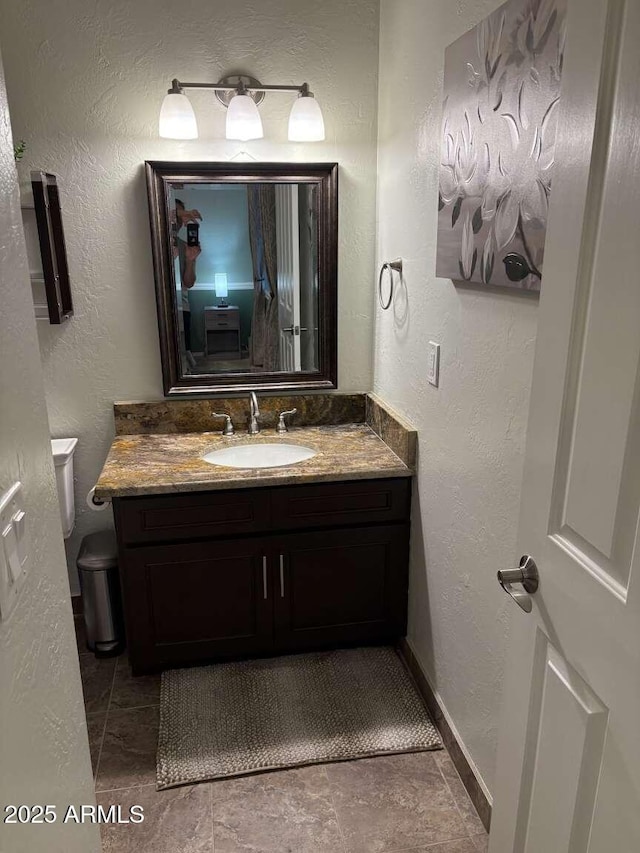 bathroom with toilet, vanity, and a textured wall