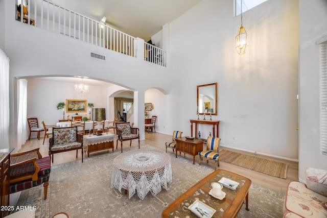 living room with visible vents, wood finished floors, arched walkways, an inviting chandelier, and a towering ceiling