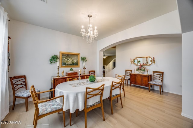 dining space with light wood-type flooring, arched walkways, baseboards, and ceiling fan with notable chandelier