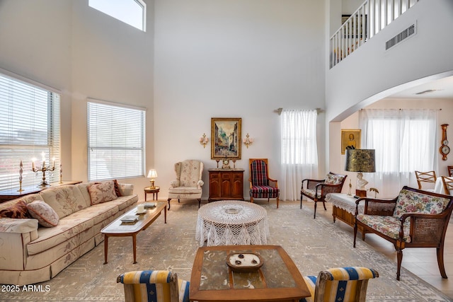 living room with a high ceiling, a healthy amount of sunlight, visible vents, and arched walkways