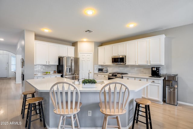 kitchen with visible vents, an island with sink, arched walkways, appliances with stainless steel finishes, and light countertops