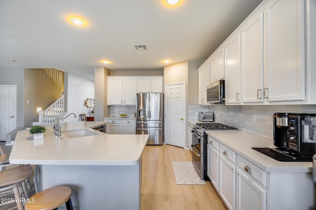 kitchen featuring visible vents, a breakfast bar, a sink, stainless steel appliances, and light wood-type flooring