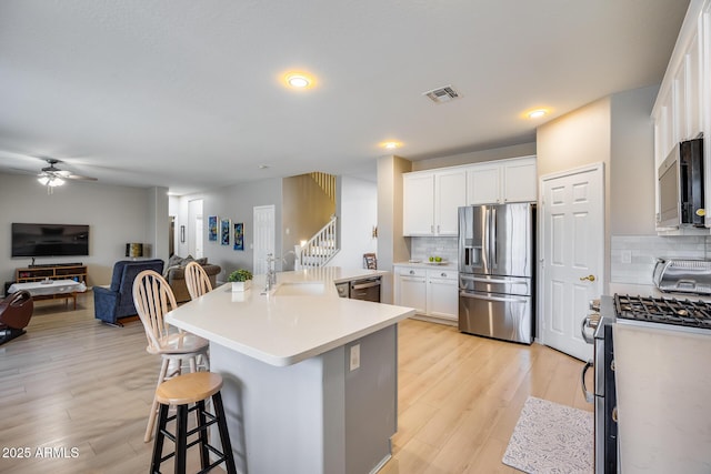 kitchen with visible vents, a breakfast bar, a sink, stainless steel appliances, and open floor plan