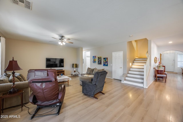 living room featuring light wood finished floors, visible vents, ceiling fan, stairway, and arched walkways