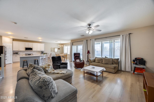 living room with ceiling fan with notable chandelier, light wood-style floors, visible vents, and a textured ceiling