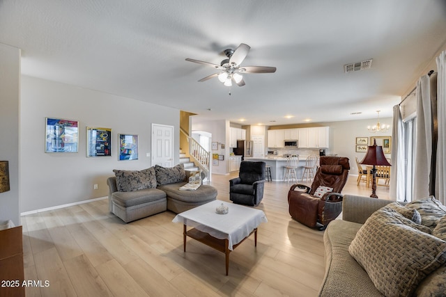 living area with stairs, ceiling fan with notable chandelier, light wood-style floors, and visible vents