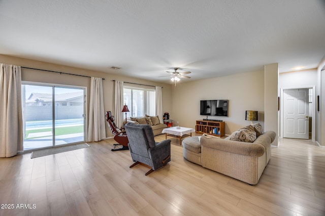 living room featuring a ceiling fan, visible vents, and light wood finished floors