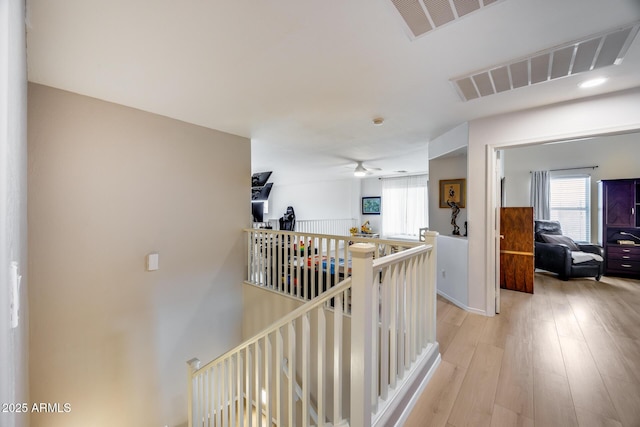 hallway with visible vents, an upstairs landing, and light wood finished floors