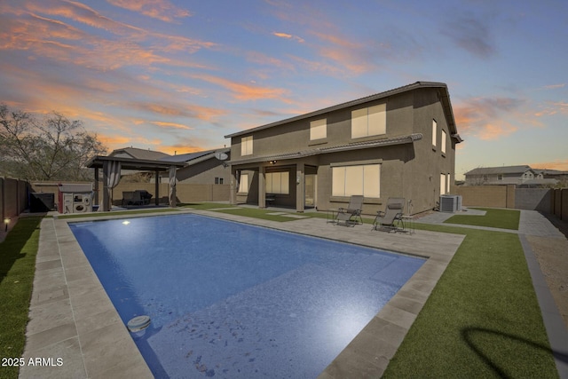 back of house at dusk with a gazebo, stucco siding, cooling unit, and a fenced backyard