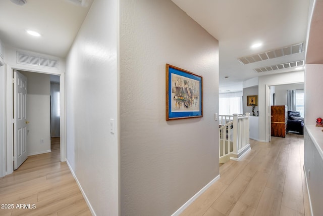 hall with an upstairs landing, visible vents, light wood finished floors, and baseboards