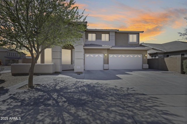 view of front of home featuring fence, concrete driveway, a tile roof, stucco siding, and a garage