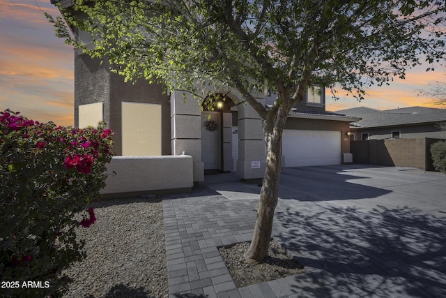 view of front facade featuring stucco siding, an attached garage, concrete driveway, and fence