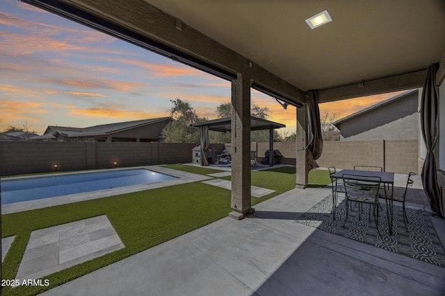 patio terrace at dusk with a fenced in pool, a lawn, a fenced backyard, and outdoor dining space