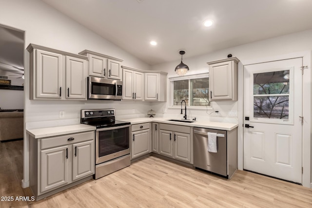 kitchen with gray cabinetry, sink, light hardwood / wood-style floors, vaulted ceiling, and appliances with stainless steel finishes