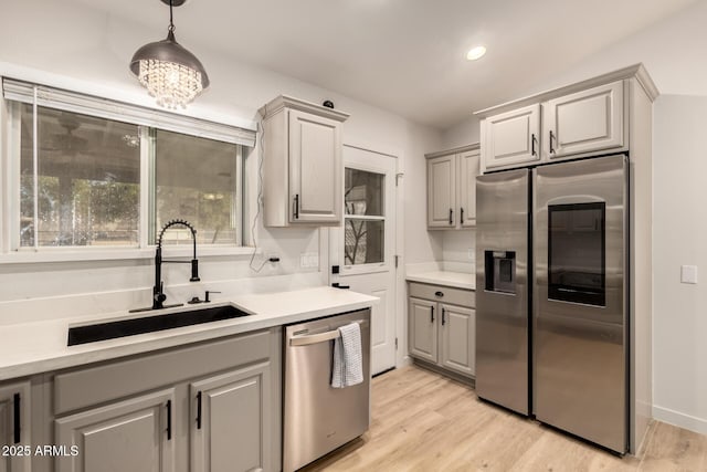 kitchen with appliances with stainless steel finishes, gray cabinetry, sink, pendant lighting, and light hardwood / wood-style floors