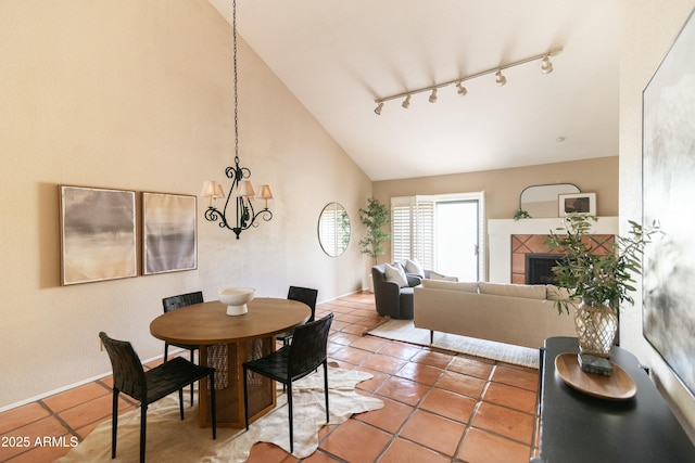 dining room featuring a notable chandelier, track lighting, a tiled fireplace, vaulted ceiling, and tile patterned floors