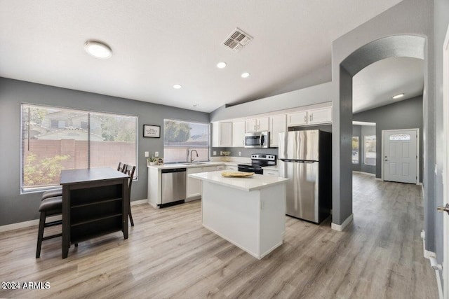 kitchen with a center island, vaulted ceiling, appliances with stainless steel finishes, a wealth of natural light, and white cabinets