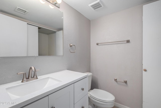 half bathroom with a textured wall, visible vents, toilet, and vanity