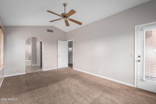 unfurnished bedroom featuring vaulted ceiling, light carpet, baseboards, visible vents, and arched walkways