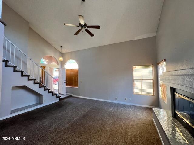 unfurnished living room with ceiling fan, dark colored carpet, and high vaulted ceiling