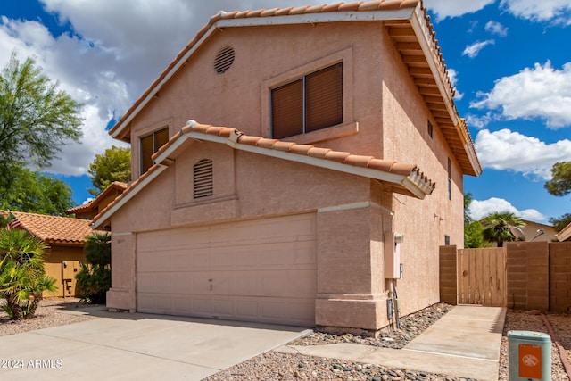 view of front facade with a tile roof, stucco siding, fence, an attached garage, and driveway