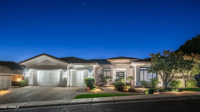 prairie-style house with a garage, decorative driveway, and stucco siding