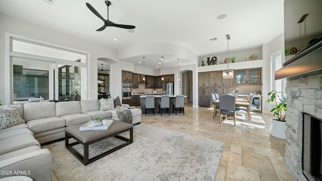 122 E Desert Wind Dr, Phoenix, AZ 85048 - living room featuring arched walkways, recessed lighting, stone tile flooring, a ceiling fan, and a stone fireplace