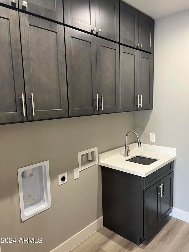 laundry room featuring electric dryer hookup, sink, cabinets, and light hardwood / wood-style flooring