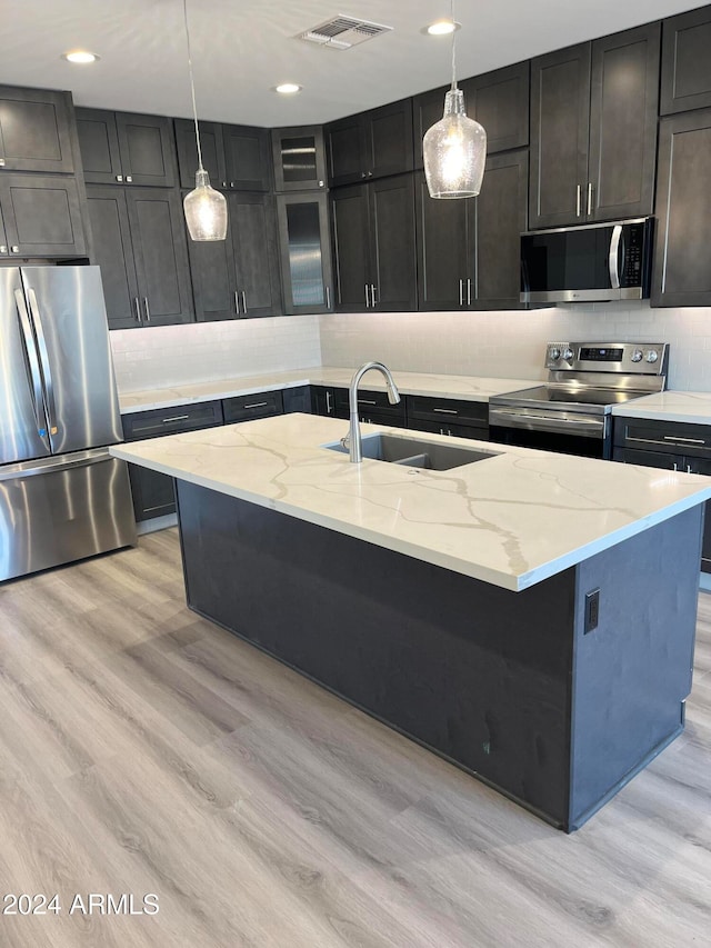 kitchen featuring sink, light hardwood / wood-style floors, pendant lighting, a center island with sink, and appliances with stainless steel finishes