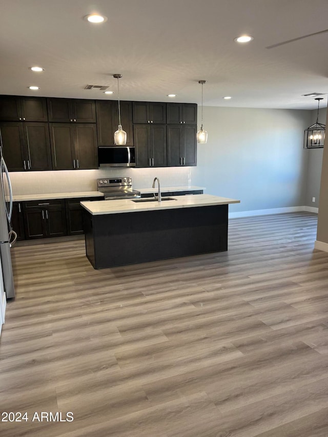 kitchen featuring pendant lighting, light wood-type flooring, stainless steel appliances, and a kitchen island with sink