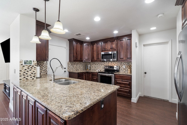 kitchen with sink, light stone counters, decorative light fixtures, appliances with stainless steel finishes, and kitchen peninsula