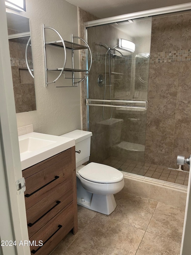 bathroom featuring tile patterned floors, vanity, toilet, and a shower with door