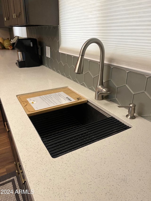 room details featuring dark brown cabinets, light stone counters, decorative backsplash, and sink