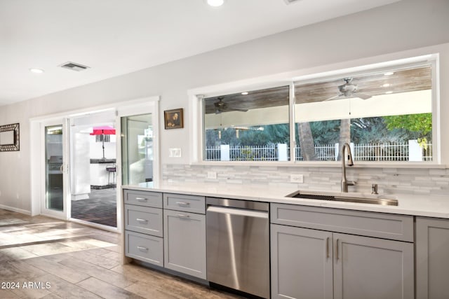 kitchen with gray cabinets, light hardwood / wood-style floors, stainless steel dishwasher, and sink