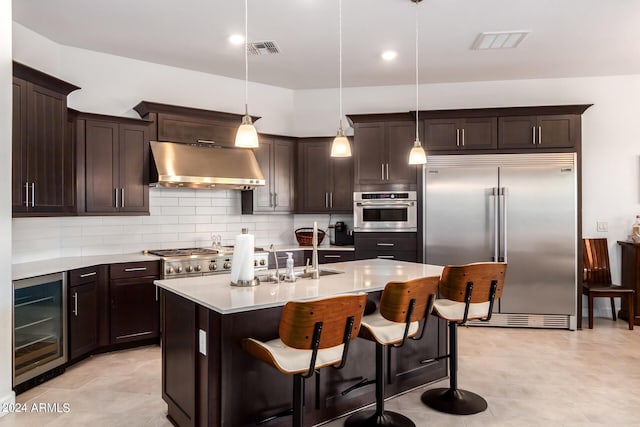 kitchen featuring wall chimney range hood, hanging light fixtures, appliances with stainless steel finishes, backsplash, and wine cooler