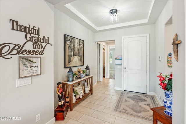 entryway featuring light tile patterned floors, a tray ceiling, and baseboards