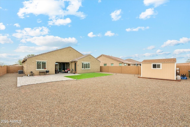 rear view of property with stucco siding, a fenced backyard, an outdoor structure, a storage unit, and a patio