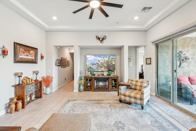 interior space featuring a tray ceiling, visible vents, baseboards, and a glass covered fireplace