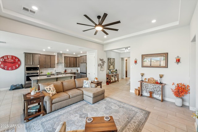 living area with a tray ceiling, baseboards, visible vents, and ceiling fan