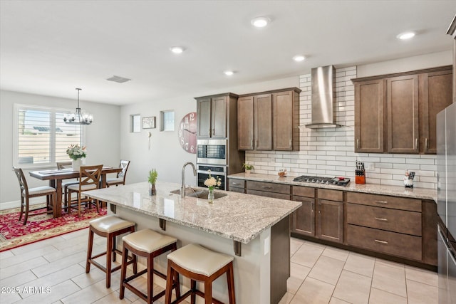 kitchen featuring a breakfast bar, a sink, backsplash, stainless steel appliances, and wall chimney range hood