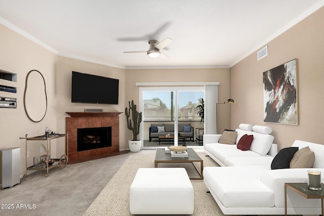 carpeted living room featuring a tiled fireplace, ceiling fan, and crown molding