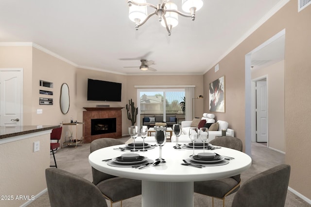 dining room featuring light carpet, crown molding, a tiled fireplace, and ceiling fan with notable chandelier