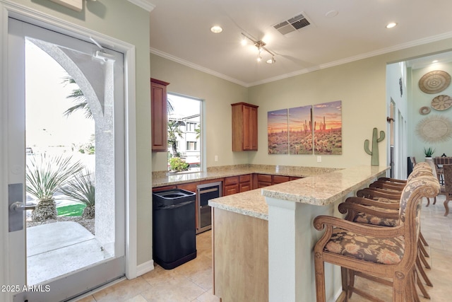 kitchen with beverage cooler, visible vents, a breakfast bar area, ornamental molding, and a peninsula