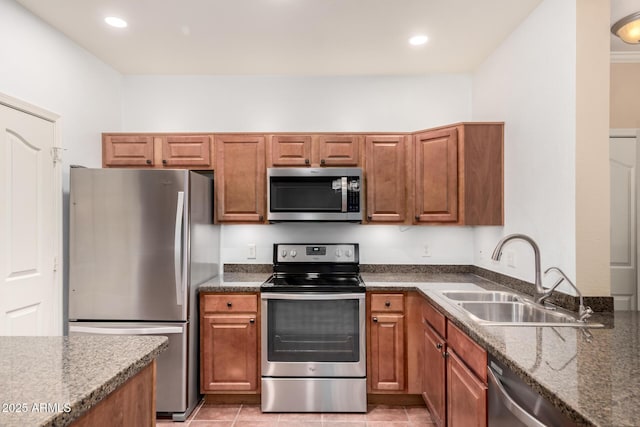 kitchen with stainless steel appliances, dark stone counters, brown cabinetry, and a sink