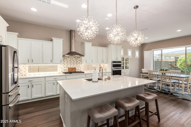 kitchen featuring appliances with stainless steel finishes, wall chimney exhaust hood, a chandelier, decorative backsplash, and recessed lighting