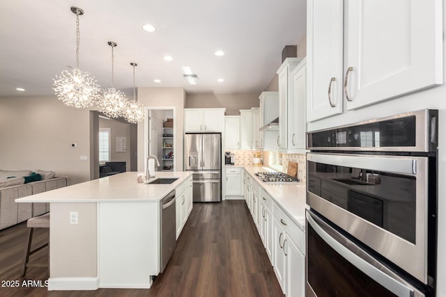 kitchen featuring stainless steel appliances, a sink, open floor plan, light countertops, and dark wood-style floors